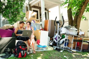 Photo of two undergraduates surrounded by their possessions on the lawn of their campus-area rental house during the annual Madison move-out/move-in weekend.