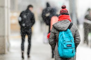 Students wearing winter clothes walk down University Avenue as snow falls.