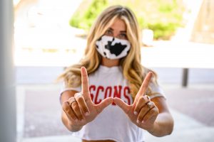 A student wearing a face mask makes the Wisconsin W sign with her hands.