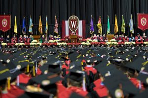 The view from the graduates' perspective of Chancellor Blank on the winter Commencement stage, lined with poinsettias and banners.