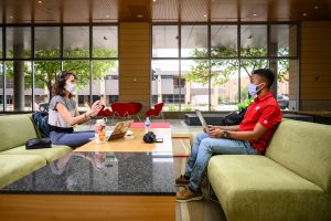 Two students, socially distanced and wearing face masks, study on couches in the Discovery Building at UW-Madison.