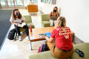 Wearing face masks and maintaining physical distance, three undergraduate students study in the Discovery Building atrium.