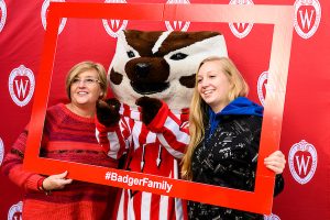 A mother and daughter pose with Bucky in a picture frame with the hashtag Badger Family.