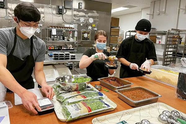 Three students work to package food in a commercial kitchen.