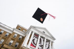 Tossed in the air, a graduation mortarboard and cap tassel floats through the sky in front of Bascom Hall