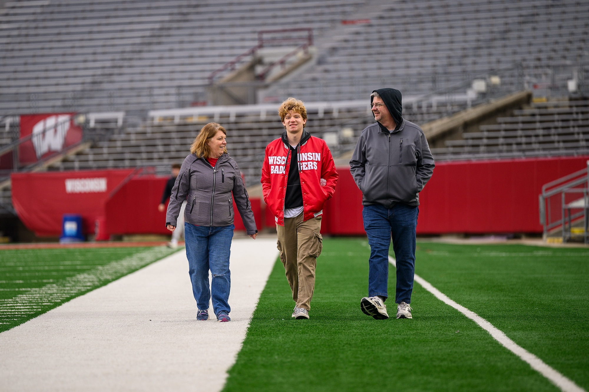At center, second-year undergraduate Christopher Conkle walks with is parents Ed and Karen Conkle from Illinois walk together during a Family Weekend photos on the field event at Camp Randall Stadium.