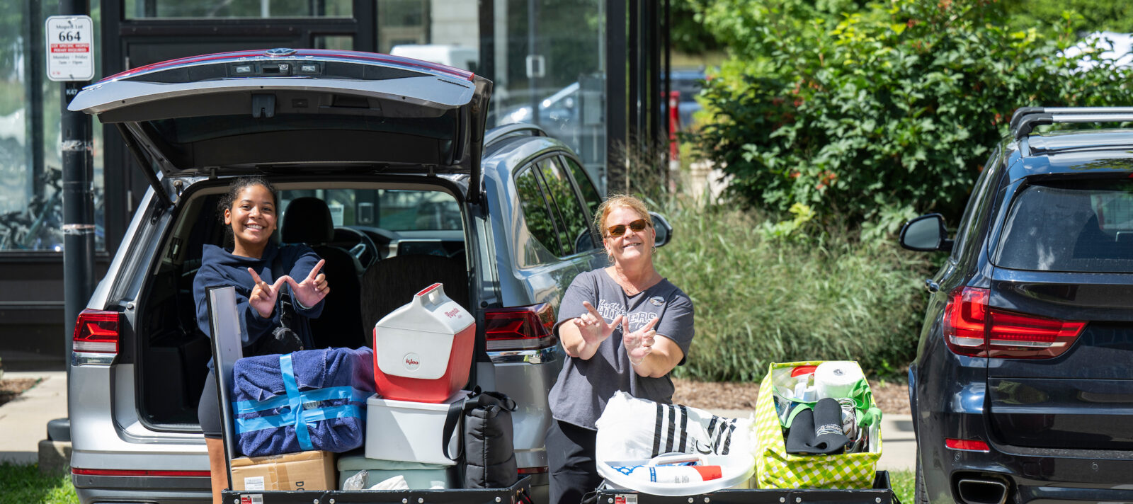 A student and her mom hold up a W next to their car during move in