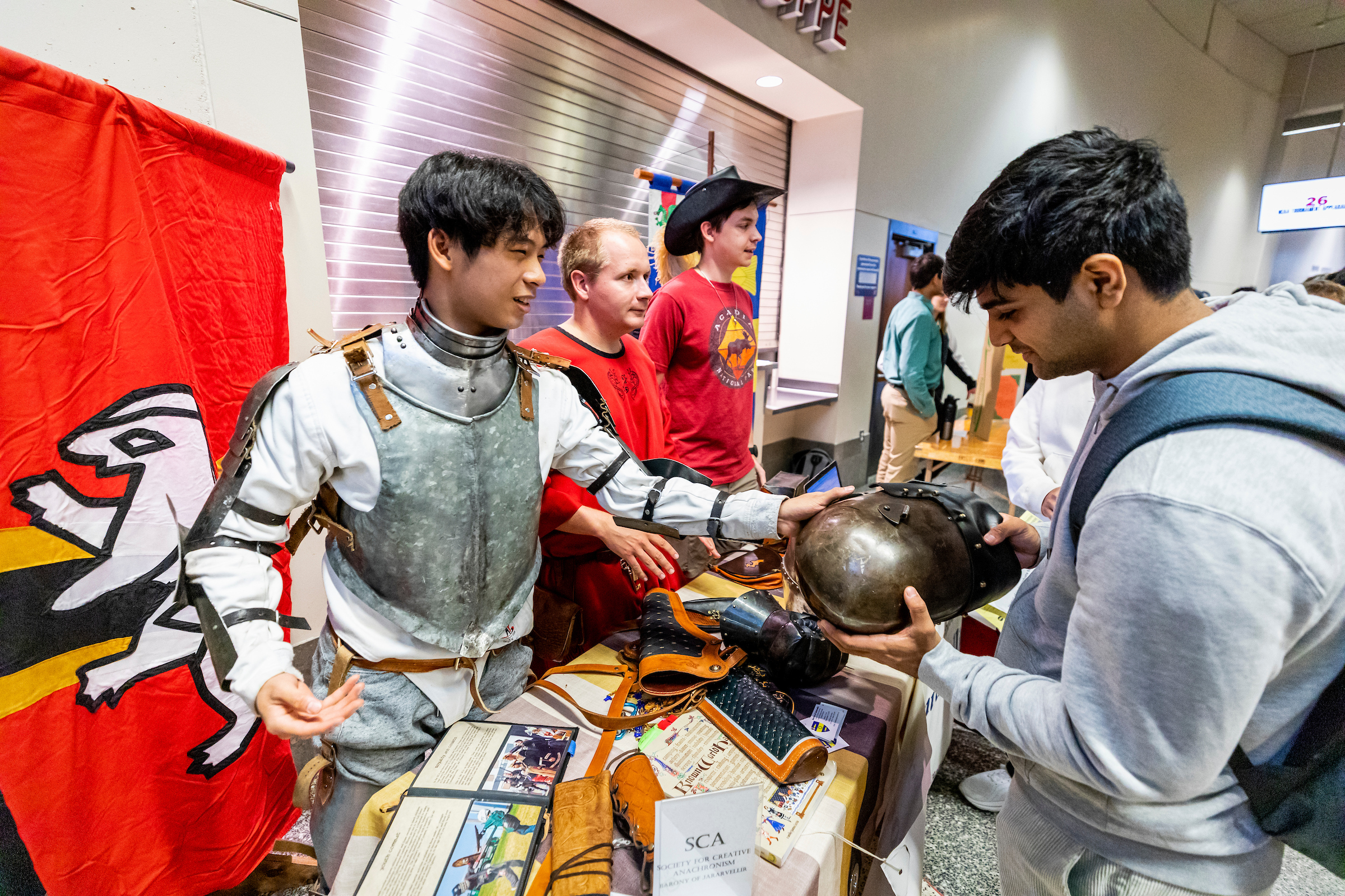 A club member in armor shows an interested student a piece of the armor. 