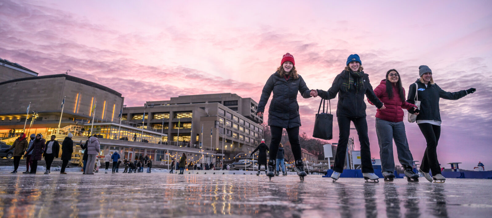 Students skate on frozen lake Mendota near Memorial Union at twilight